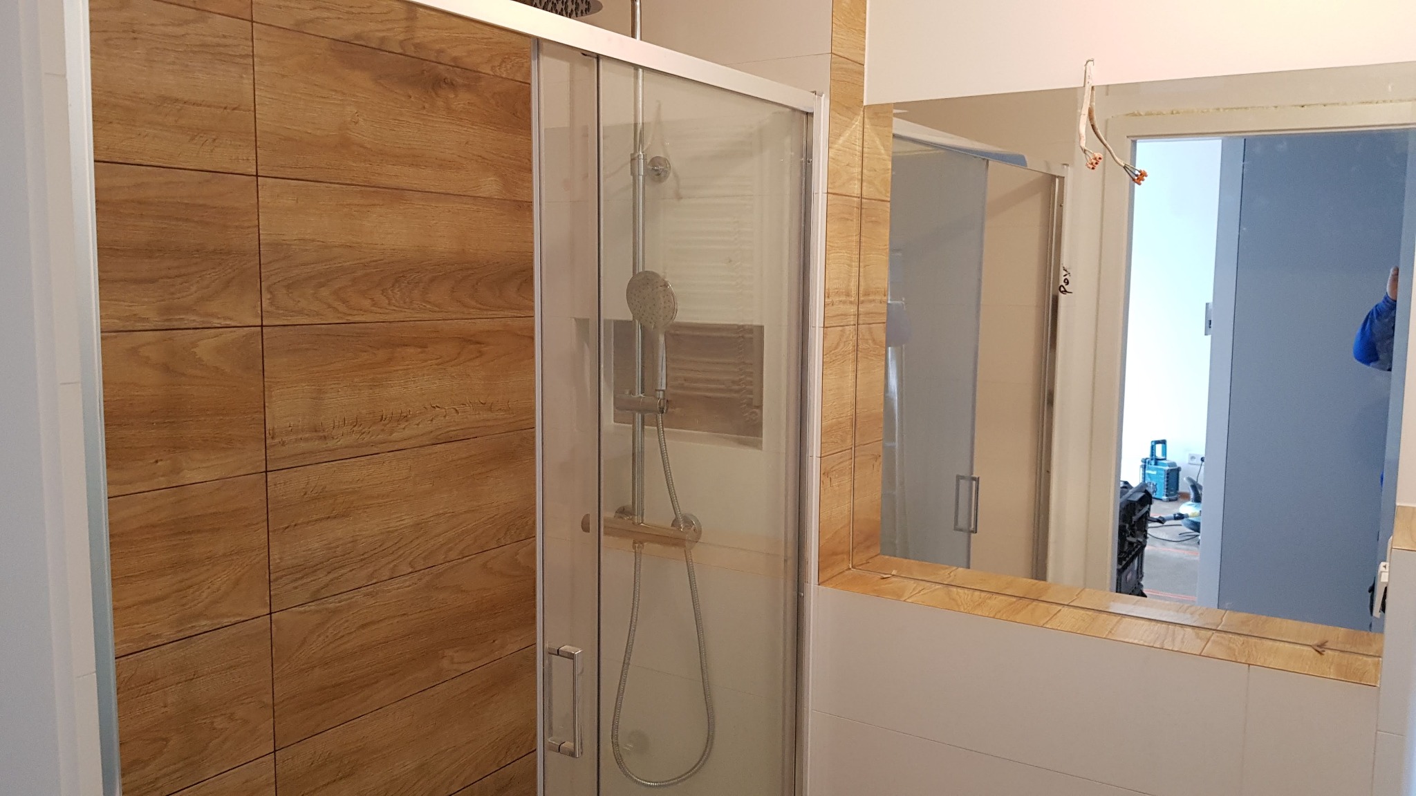 Wykończona kabina prysznicowa z przesuwnymi drzwiami, obudowana płytkami imitującymi drewno, widok z lustra z fragmentem instalacji elektrycznej
