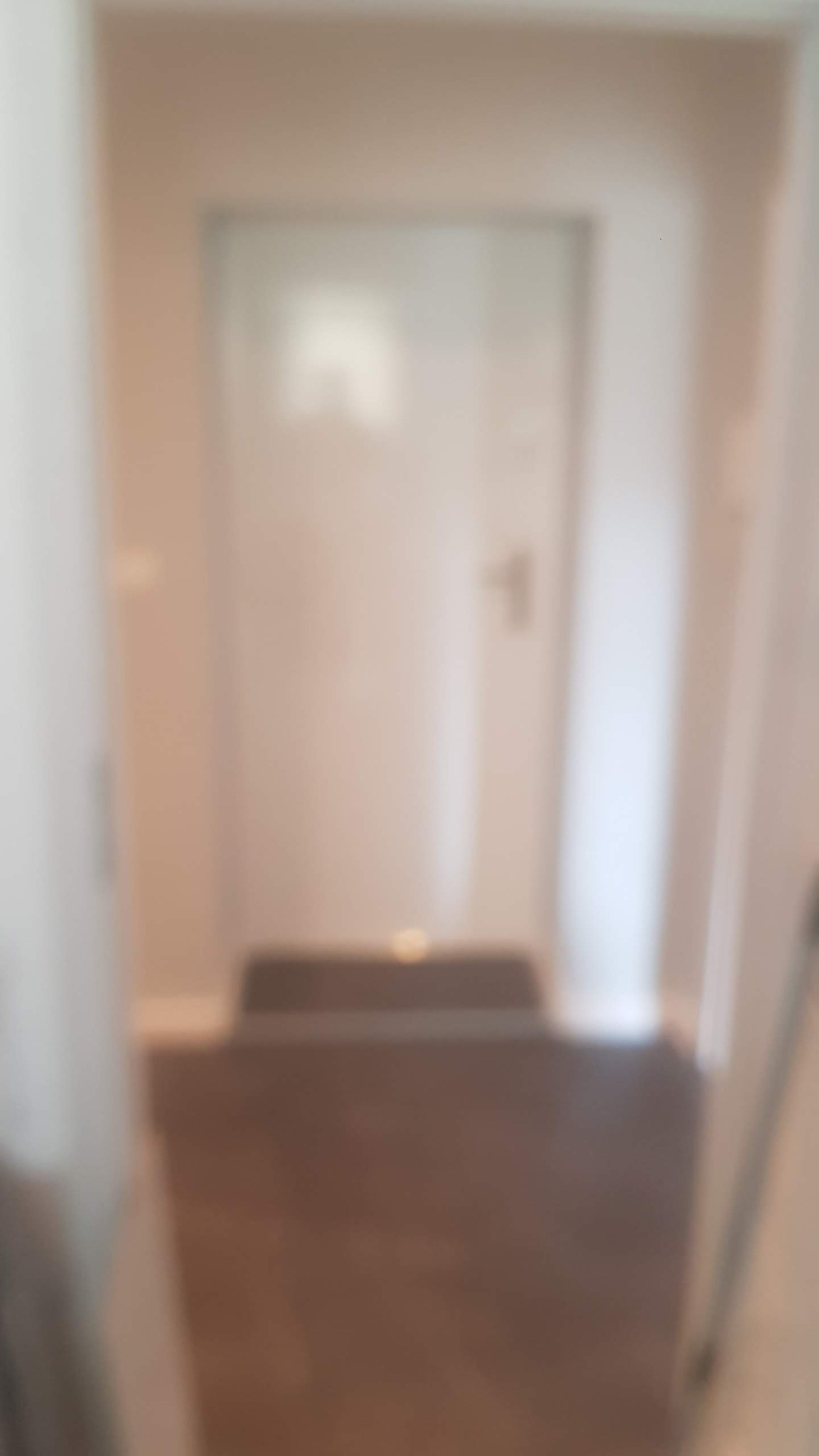 Rozmazane ujęcie korytarza z ciemną podłogą i białymi ścianami, w tle białe drzwi z numerem 1.