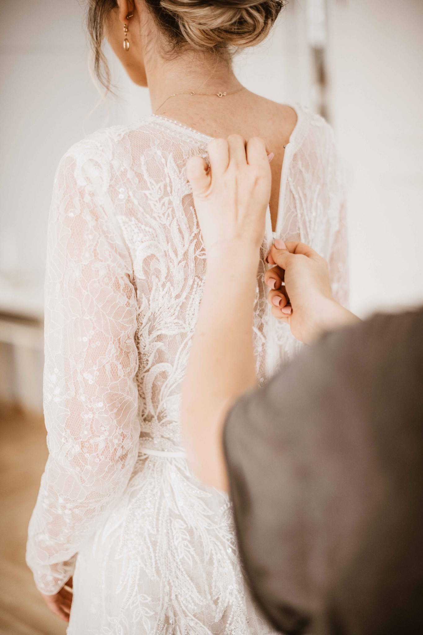 Zapinanie sukni ślubnej z koronkowym wzorem na plecach panny młodej, widok z tyłu, delikatna biżuteria.