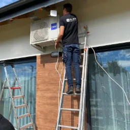 Mężczyzna na drabinie montuje klimatyzator Haier na elewacji domu, widoczne narzędzia i logo firmy na koszulce.