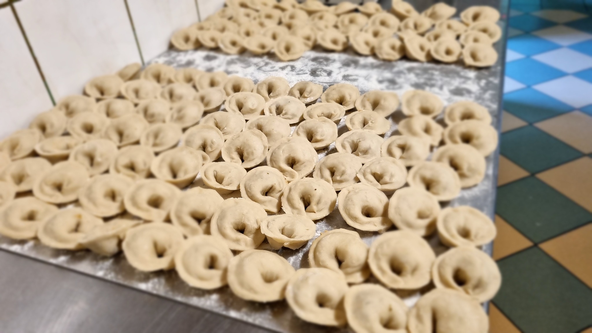 Ręcznie lepione pierogi, ułożone na posypanej mąką, metalowej powierzchni roboczej przed gotowaniem.