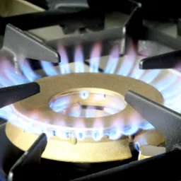 Palnik kuchenki gazowej z płomieniem, widok z bliska, czarne ruszty, złoty palnik, błękitny płomień.