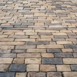 Ułożona kostka brukowa w odcieniach szarości i beżu, tworząca wzór na podjeździe lub chodniku, z perspektywą z dołu.