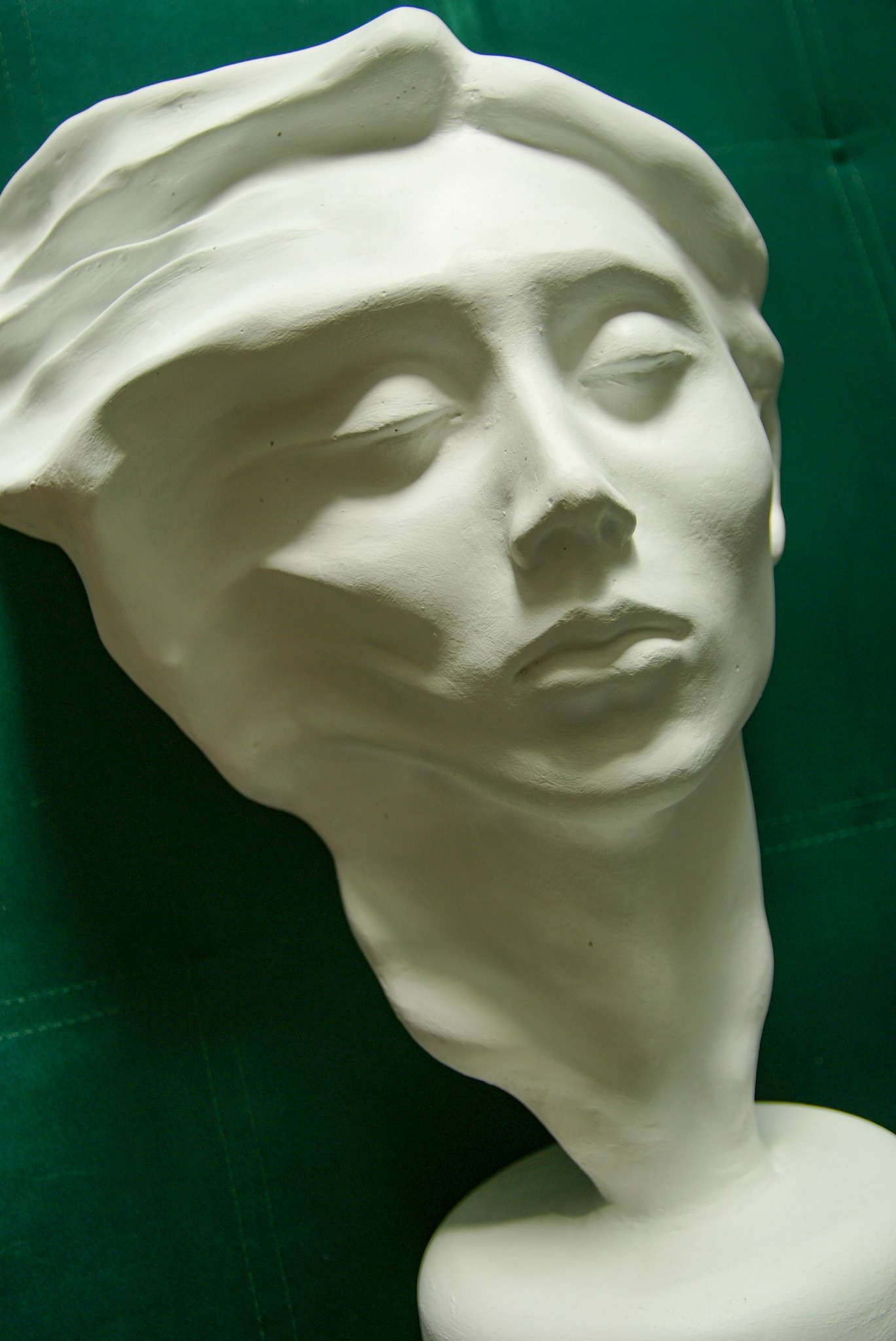 Gipsowy odlew głowy kobiety z zamkniętymi oczami na tle zielonego materiału.