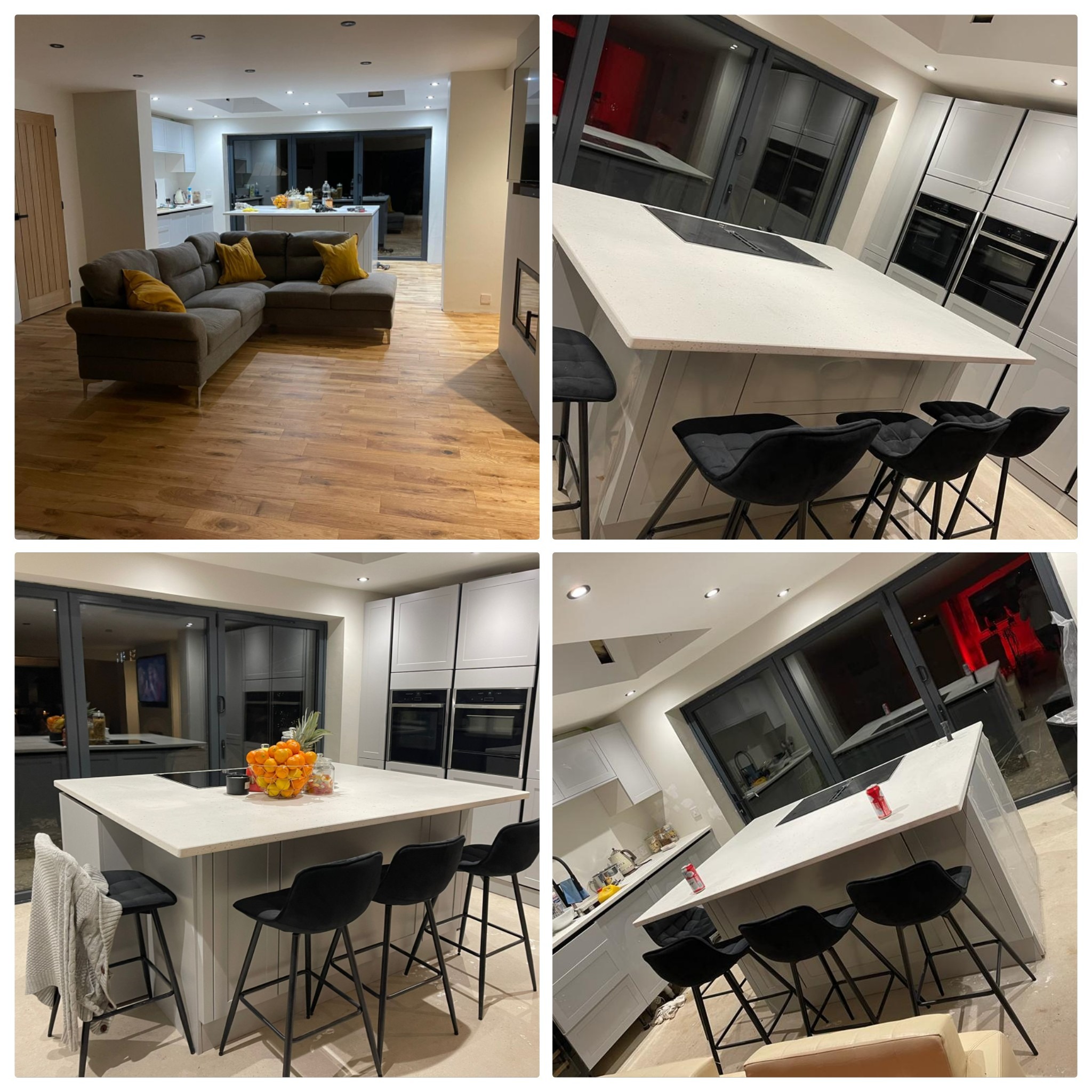 Nowoczesne wnętrze domu z otwartą kuchnią i salonem, drewniana podłoga, szary narożnik z żółtymi poduszkami, wyspa kuchenna z czarnymi hokerami i białym blatem, duże okno przesuwne.