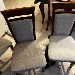 Pogromcy Plam Michał Adamczyk - Dwa krzesła z tapicerowanymi siedziskami i oparciami o delikatnym wzorze, stojące na kafelkowej podłodze, obok widoczny fragment stołu i butelka z rozpylaczem w tle.