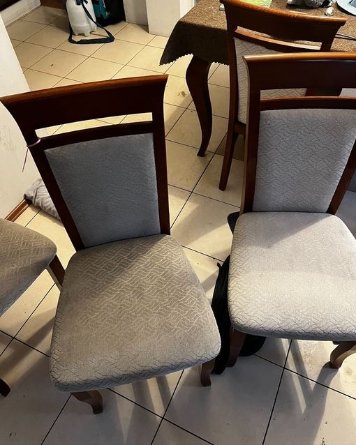 Dwa krzesła z tapicerowanymi siedziskami i oparciami o delikatnym wzorze, stojące na kafelkowej podłodze, obok widoczny fragment stołu i butelka z rozpylaczem w tle.