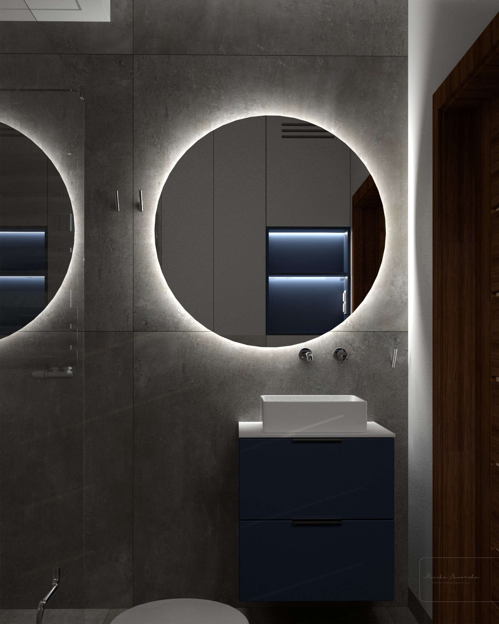 Nowoczesna łazienka z podświetlanym okrągłym lustrem, umywalką nablatową na szafce w kolorze granatowym i szarymi płytkami imitującymi beton na ścianach.