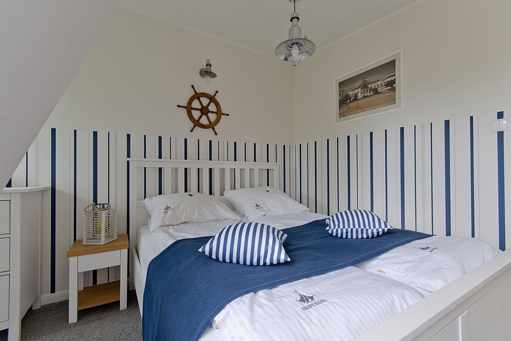 Pokój w stylu marynistycznym w Sopocie: białe meble, ściany w biało-niebieskie pasy, dekoracyjne koło sterowe i lampa w stylu retro.