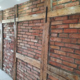 Usługi Ogólnobudowlane Paweł Krawczyk - Ceglana ściana wewnętrzna z drewnianą konstrukcją szkieletową, widoczne ślady napraw i renowacji, oświetlenie sufitowe.