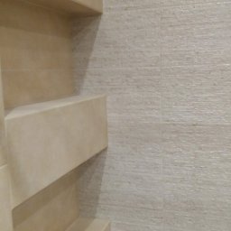 Ameliizlat Team - Beżowe półki wbudowane w ścianę pokrytą płytkami o drobnej, poziomej fakturze, tworzące minimalistyczny i funkcjonalny element wystroju wnętrza.