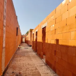 Budowa budynku handlowego w Gorzycach. Murowane ściany z pustaków ceramicznych tworzą korytarz z otworami okiennymi i drzwiowymi. Widok w perspektywie.