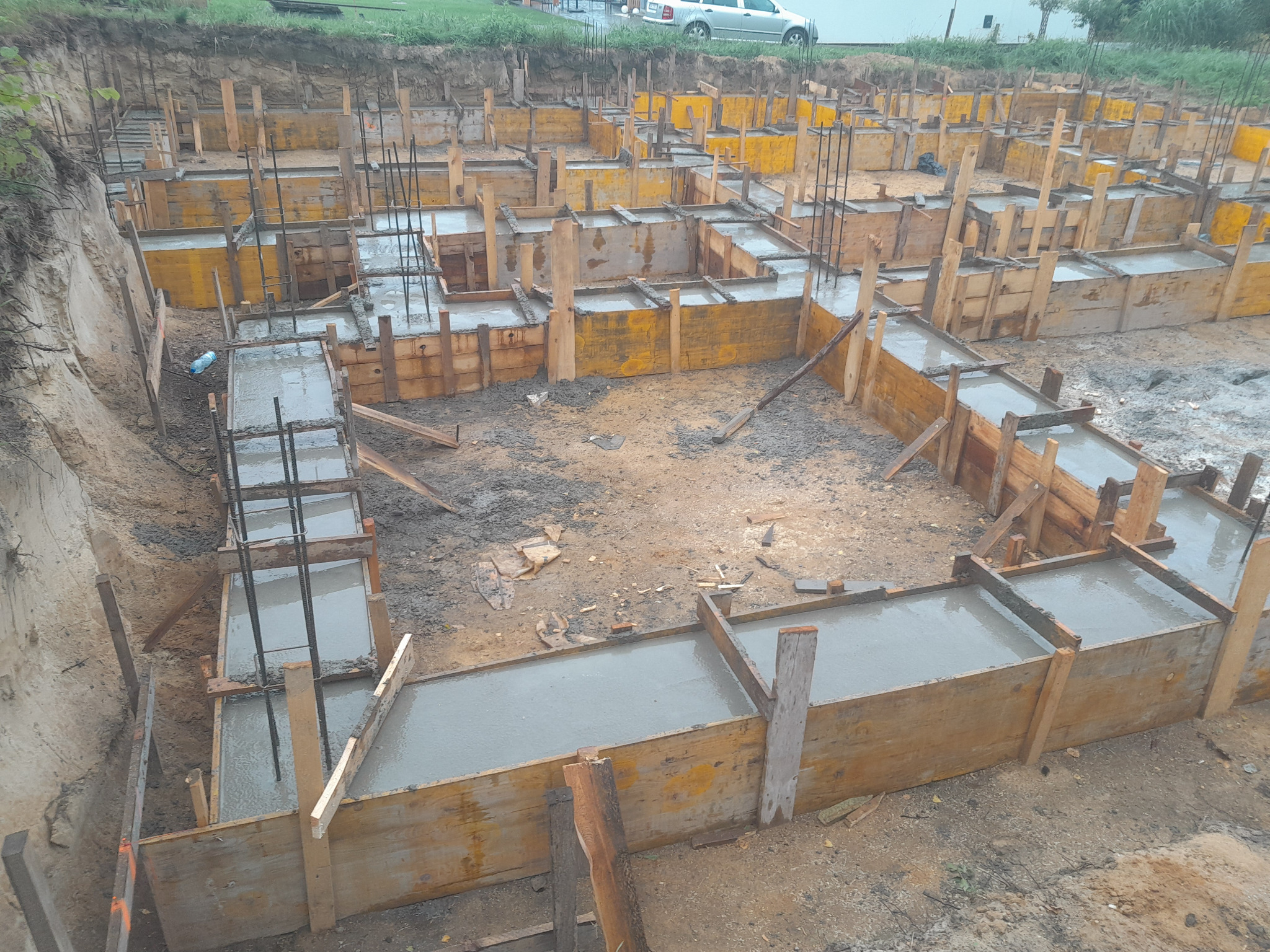 Zalane betonem ławy fundamentowe w drewnianym szalunku z wystającymi prętami zbrojeniowymi, widok z góry na plac budowy domu jednorodzinnego.
