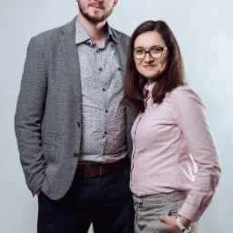 Portret dwojga uśmiechniętych pracowników w swobodnych strojach biznesowych na jasnym tle.