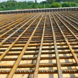 Siatka z prętów zbrojeniowych, przygotowana do zalania betonem, widoczna na budowie w Łączanach. Elementy dystansowe z tworzywa sztucznego utrzymują odpowiedni odstęp od podłoża.