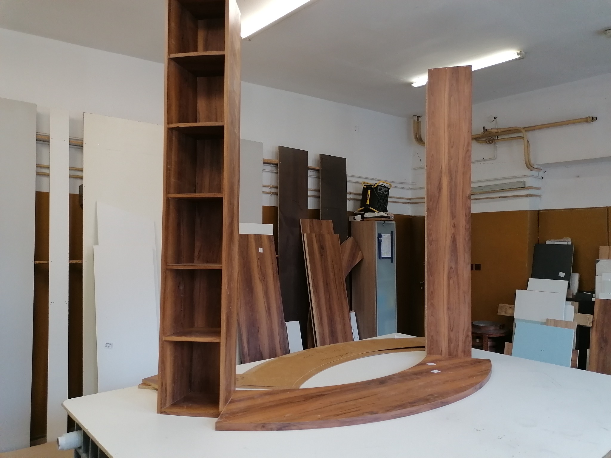 Elementy szafy na wymiar z forniru orzechowego w warsztacie stolarskim: regał z półkami, pionowy panel i zaokrąglony blat, przygotowane do montażu.