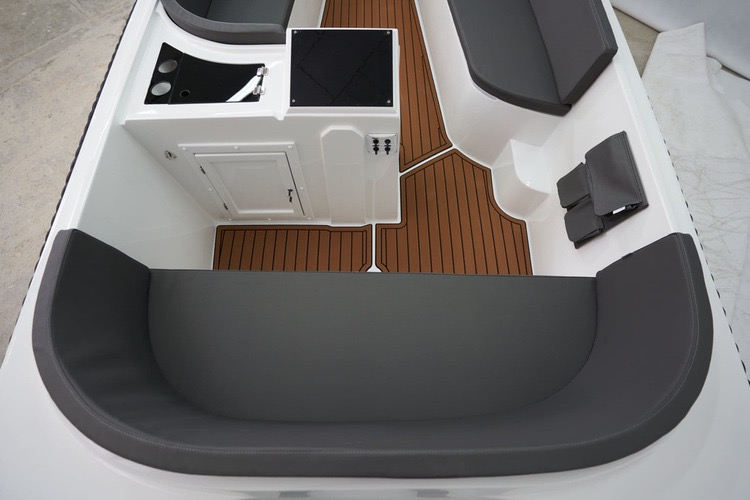 Wnętrze łodzi motorowej z szarą tapicerką, brązową podłogą imitującą drewno i białymi ścianami. Widok z góry, ukazujący detale wykończenia i wyposażenia.
