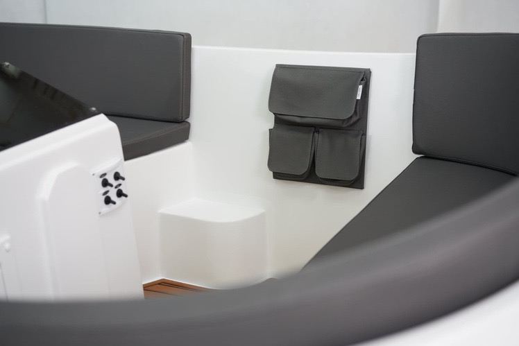 Wnętrze łodzi z szarymi tapicerowanymi siedzeniami i wiszącym, szarym organizerem z kieszeniami, zamontowanym na białej ścianie. Widoczne detale wykończenia.