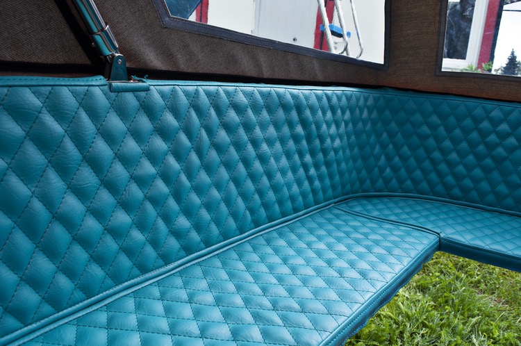 Turkusowa, pikowana tapicerka siedziska w pojeździe, widoczna z bliska. Staranne przeszycia w romby, gładka powierzchnia, fragment otoczenia w tle.