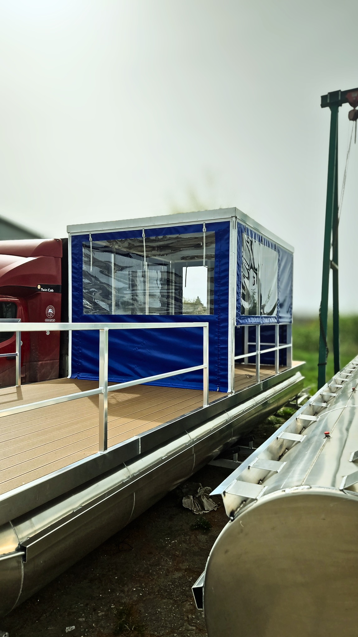 Niebieski pokrowiec z przezroczystymi oknami na łodzi, widok z boku. Metalowe elementy konstrukcyjne i drewniana podłoga pokładu.