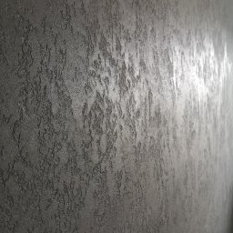 LEOPOL SPÓŁKA Z OGRANICZONĄ ODPOWIEDZIALNOŚCIĄ - Czarna ściana z dekoracyjną, chropowatą fakturą, imitującą naturalny kamień, oświetlona z boku, tworząca subtelne refleksy.