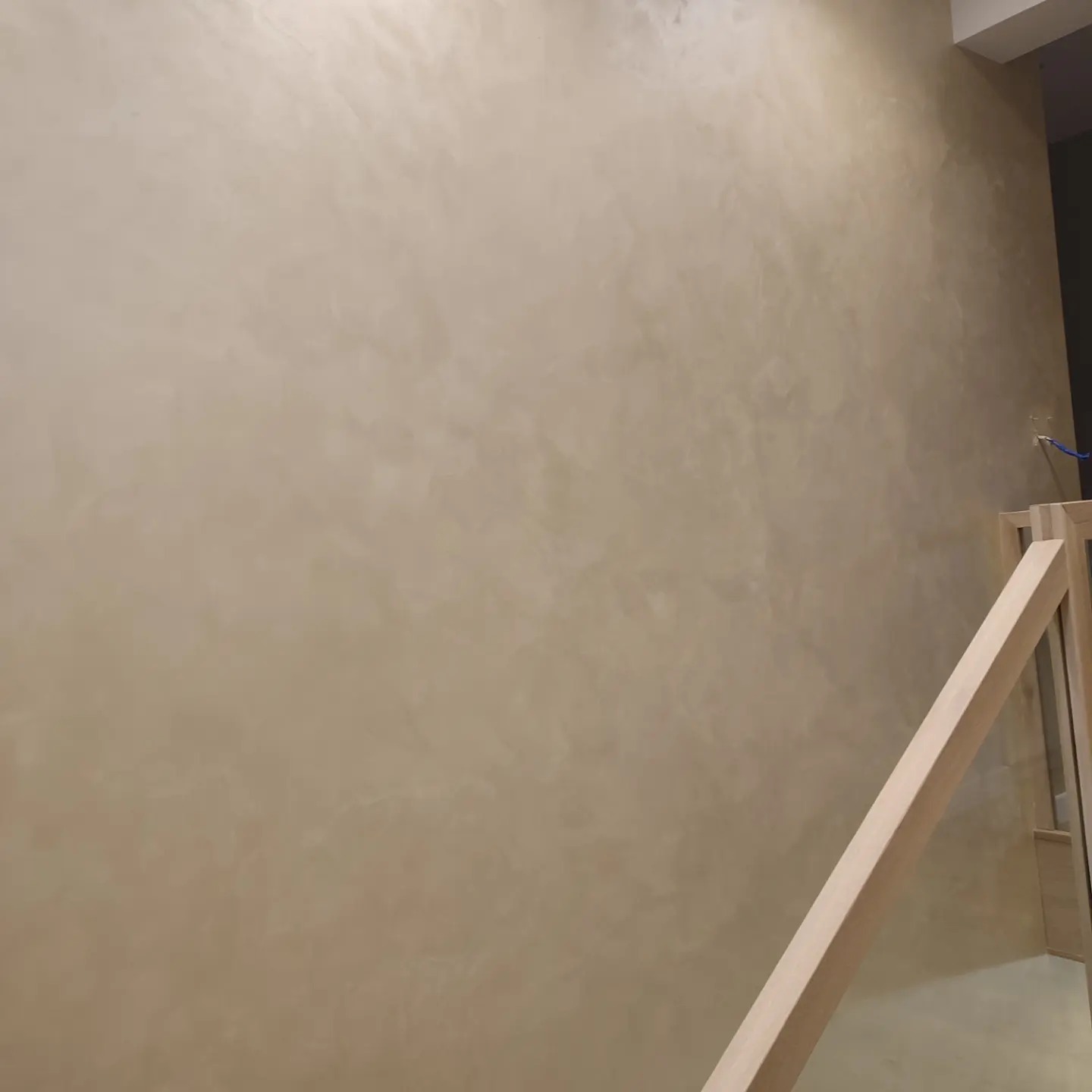 Beżowa ściana wykończona z efektem dekoracyjnym, widoczny fragment drewnianej konstrukcji w prawym dolnym rogu.