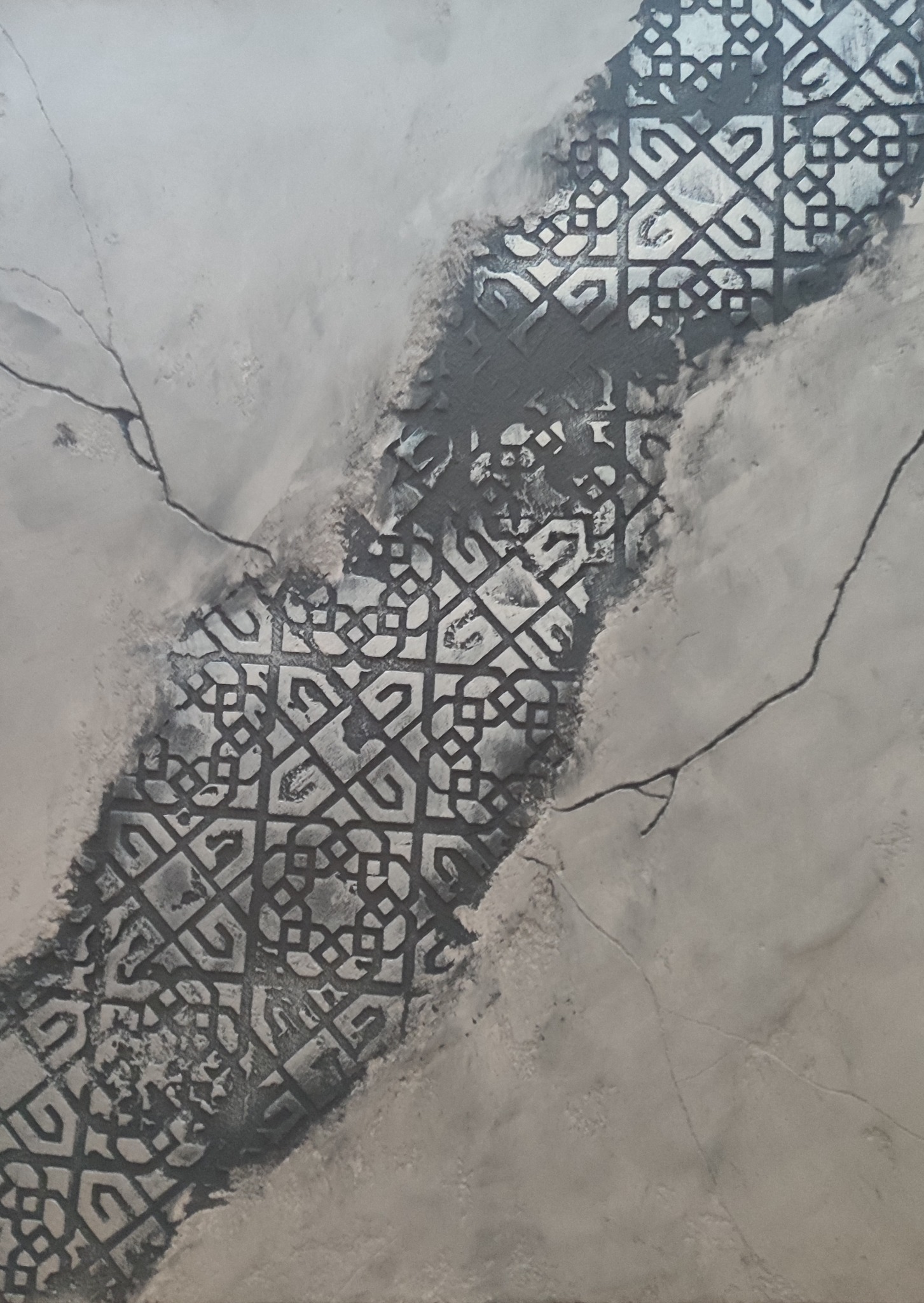 Dekoracyjna ściana z efektem spękań i wstawką z geometrycznym wzorem w odcieniach szarości.