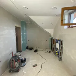 Łazienka w trakcie remontu: ściany przygotowane do malowania, zabudowa stelaża WC Geberit Duofix, widoczny odkurzacz przemysłowy i narzędzia.