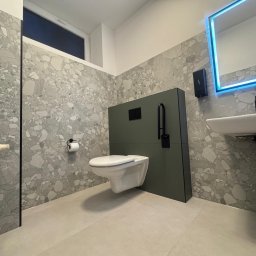 BTC-BUD Firma Remontowo-Budowlana Bartosz Chodura - Nowoczesna łazienka z szarą mozaiką na ścianach, podwieszaną toaletą na tle oliwkowozielonej zabudowy i lustrem z niebieskim podświetleniem LED.