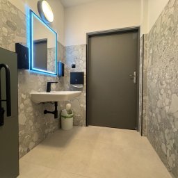 BTC-BUD Firma Remontowo-Budowlana Bartosz Chodura - Nowoczesna łazienka z umywalką, podświetlanym lustrem i szarą mozaiką na ścianach. Widoczny kosz na śmieci i uchwyt dla niepełnosprawnych. Minimalistyczny design.