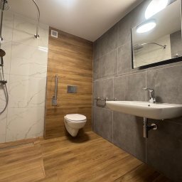 BTC-BUD Firma Remontowo-Budowlana Bartosz Chodura - Nowoczesna łazienka z kabiną prysznicową typu walk-in, umywalką nablatową i toaletą podwieszaną. Wykończenie w odcieniach szarości, bieli i drewna. Minimalistyczny design.