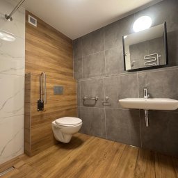BTC-BUD Firma Remontowo-Budowlana Bartosz Chodura - Nowoczesna łazienka z drewnopodobnymi i marmurowymi płytkami, wiszącą toaletą i umywalką. Udogodnienia dla osób z niepełnosprawnościami, minimalistyczny design.