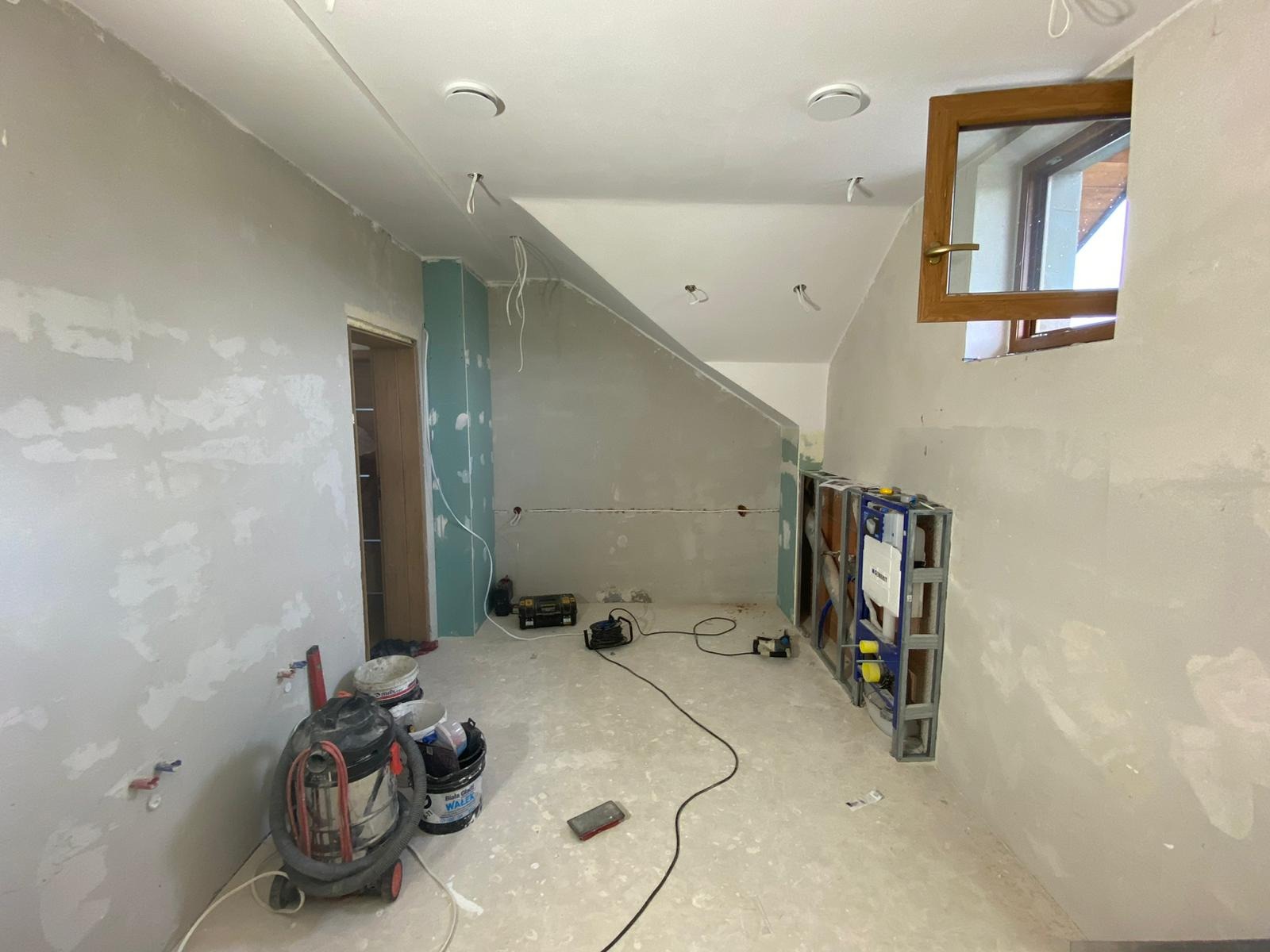 Łazienka w trakcie remontu: ściany przygotowane do malowania, zabudowa stelaża WC Geberit Duofix, widoczny odkurzacz przemysłowy i narzędzia.