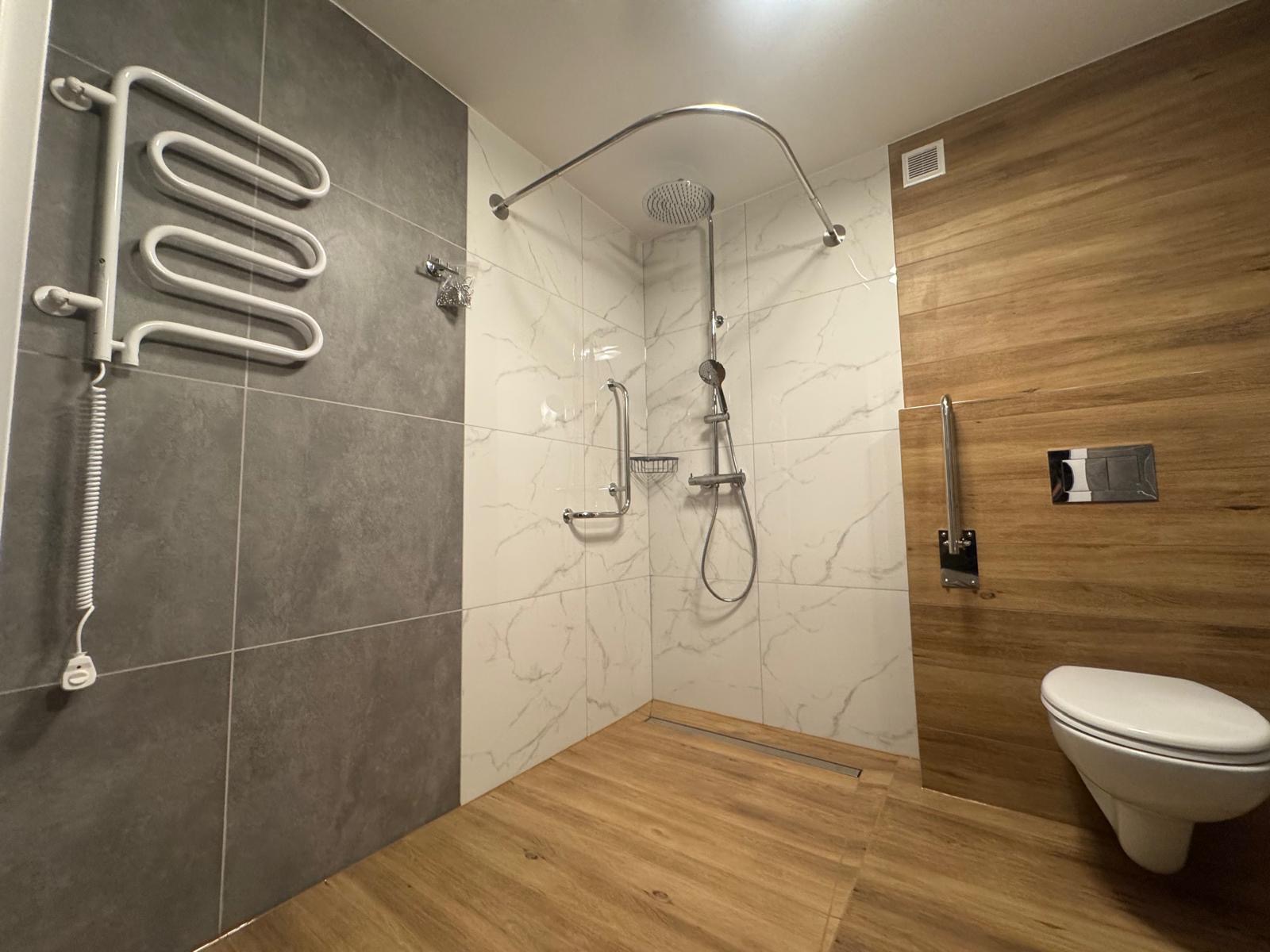 Nowoczesna łazienka po remoncie: szare i marmurowe płytki, drewnopodobna podłoga i ściana, minimalistyczna armatura, grzejnik drabinkowy.