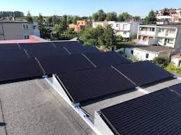 Instalacja paneli fotowoltaicznych na płaskim dachu budynku mieszkalnego, widok z góry, z widocznymi elementami montażowymi i otoczeniem miejskim.