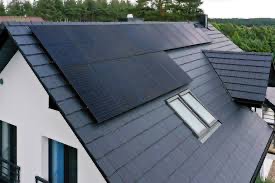 Czarny dach z panelami fotowoltaicznymi na nowoczesnym domu jednorodzinnym z oknem dachowym; widok z góry, drzewa w tle.