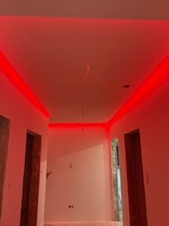 Korytarz po remoncie z oświetleniem LED w kolorze czerwonym, widoczne gładkie ściany i sufit. Otwory drzwiowe bez drzwi. Minimalistyczny design.