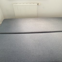 Clean-Pro - Szary, rozłożony narożnik tapicerowany w rogu pokoju, widoczny grzejnik na ścianie.