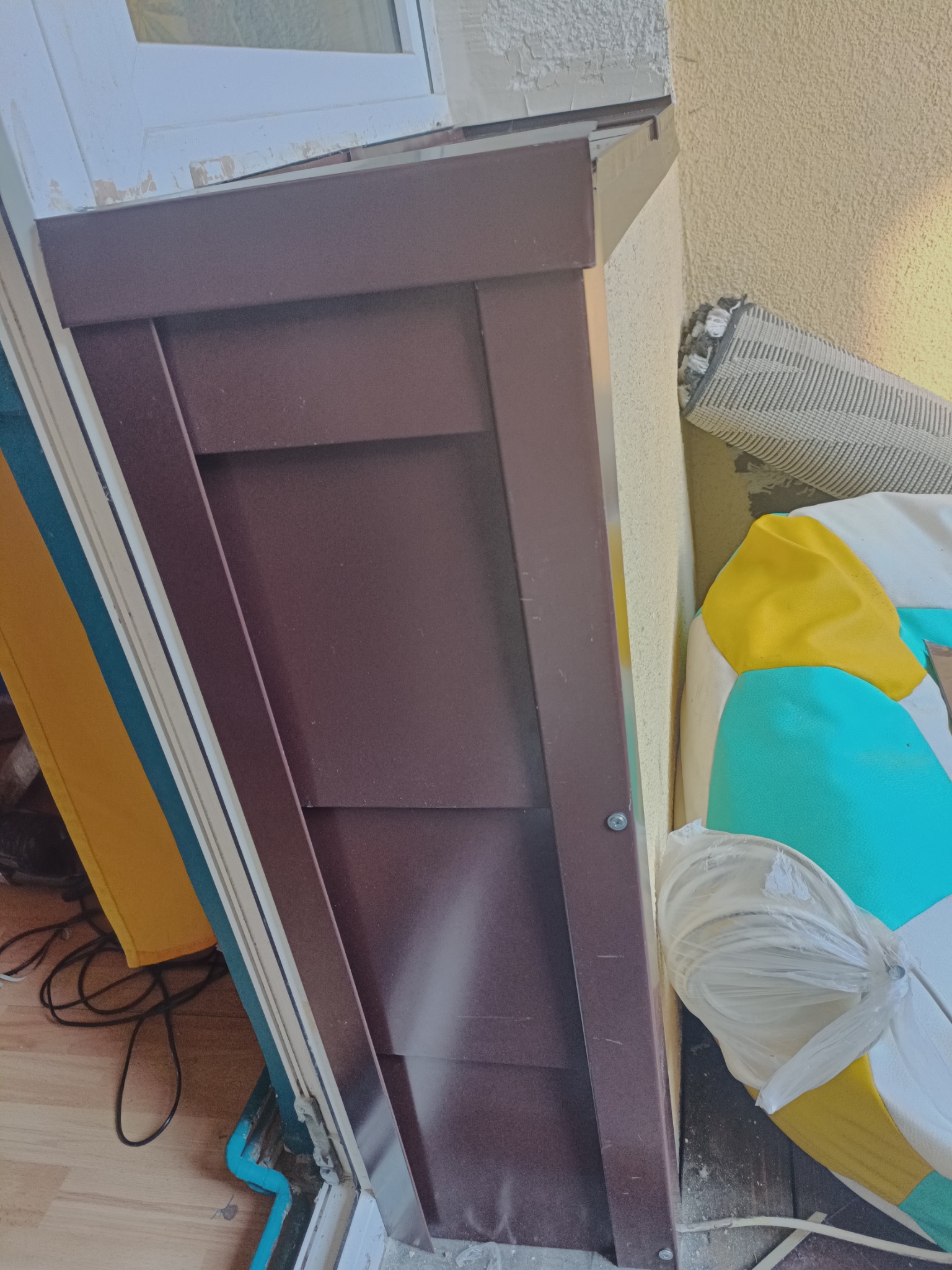 Fragment brązowej obróbki blacharskiej przy oknie, widoczne ślady farby na ścianie i elementy izolacji termicznej w tle.