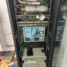 Szafa rack z zainstalowanym systemem monitoringu wizyjnego w Biłgoraju, monitor wyświetla obraz z kamer, widoczne kable i urządzenia sieciowe.