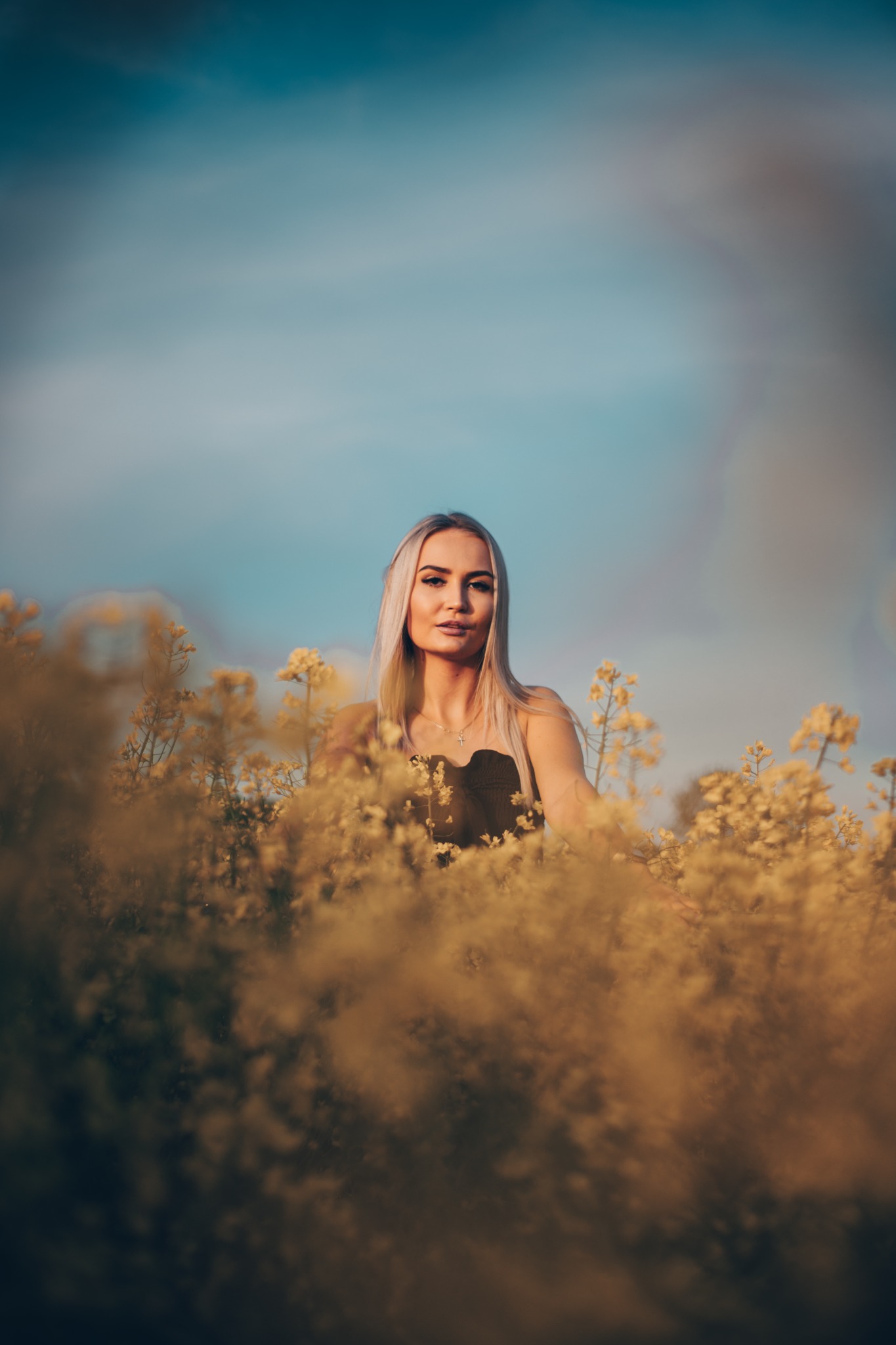 Portret kobiety z blond włosami w polu kwitnącego rzepaku, delikatne światło zachodzącego słońca