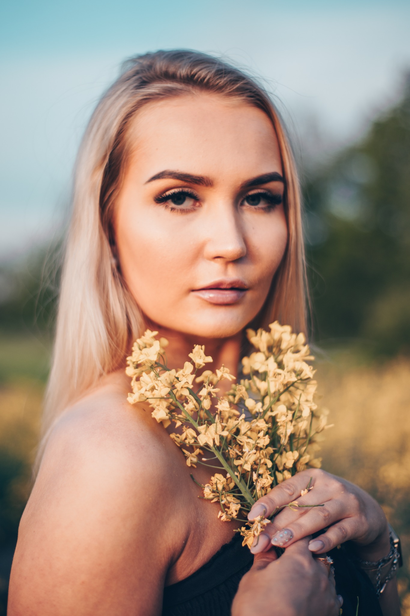 Portret kobiety z blond włosami trzymającej bukiet żółtych kwiatów na tle rozmytej zieleni