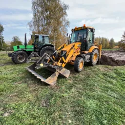 Żółta koparko-ładowarka JCB z otwartą łyżką i zielony traktor Deutz-Fahr na trawiastym terenie, obok świeżo wykopany rów ziemny.