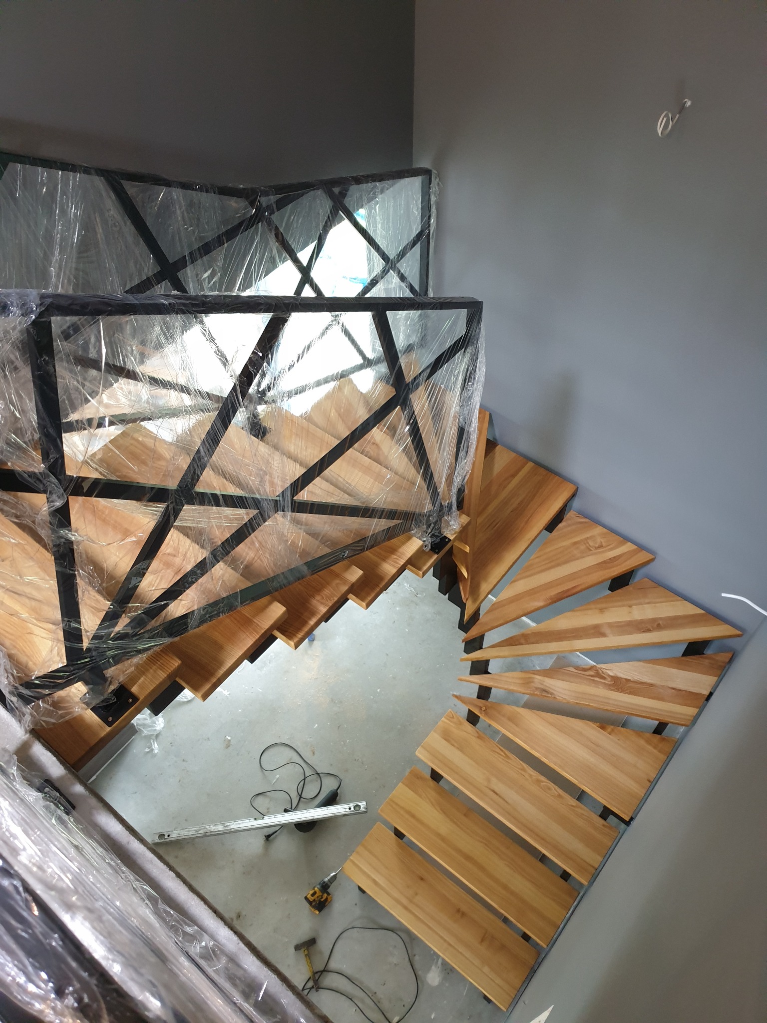 Klatka schodowa w trakcie montażu: drewniane stopnie na metalowej konstrukcji, zabezpieczona folią, widoczne narzędzia na podłodze.