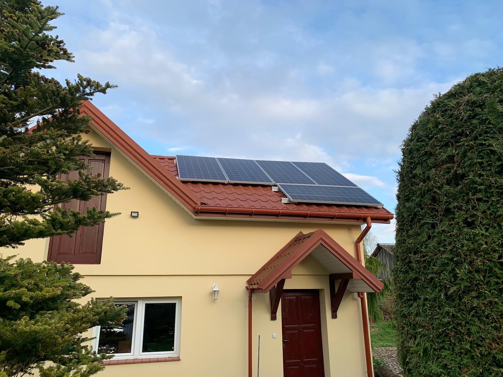 Instalacja paneli słonecznych na dachu domu jednorodzinnego w Przasnyszu, widok z poziomu gruntu, zieleń w tle.