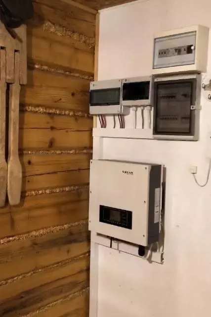 Wnętrze drewnianego domu z zainstalowanym inwerterem i rozdzielnicą elektryczną, widoczne okablowanie.