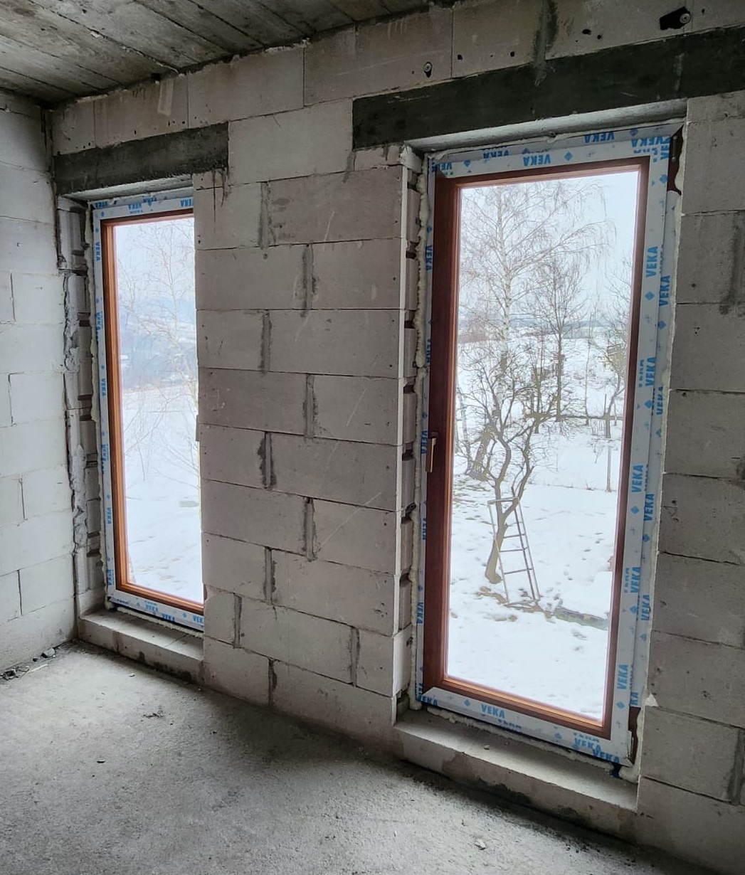 Montaż okien PCV z profilem VEKA w surowym stanie, widoczne bloczki betonowe i zimowy krajobraz za oknem.