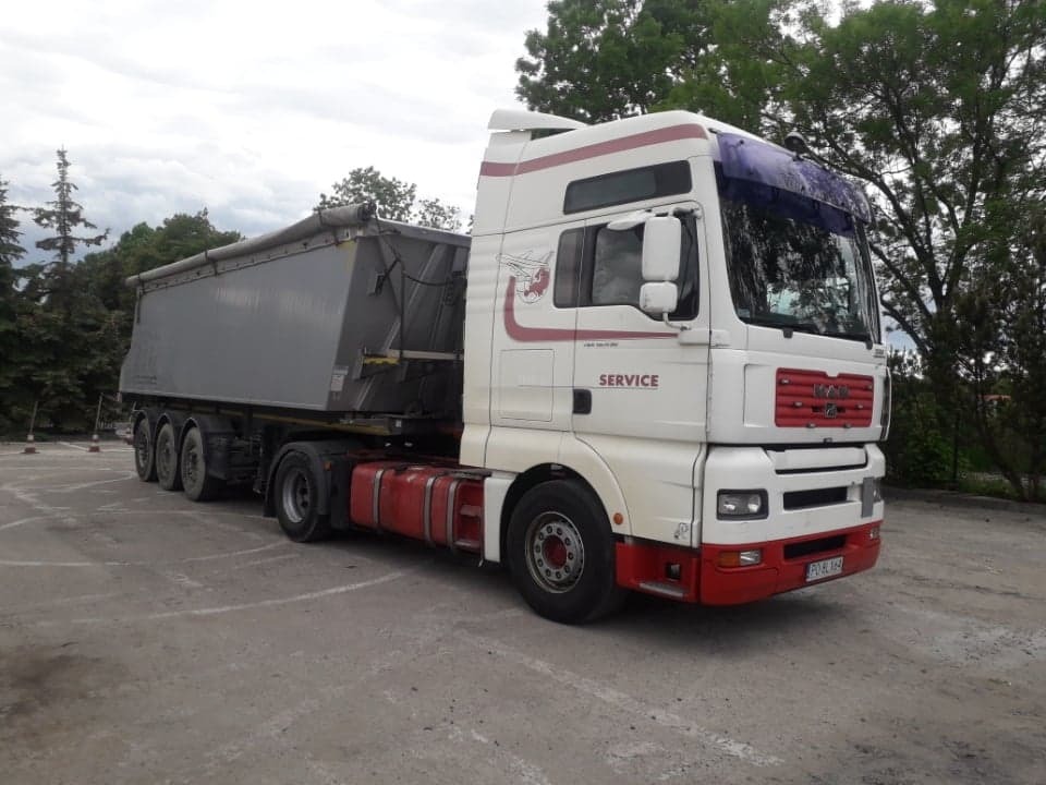 Ciężarówka MAN z naczepą wywrotką na parkingu, widoczne oznaczenia 'SERVICE' i czerwone akcenty na białej kabinie, drzewa w tle.