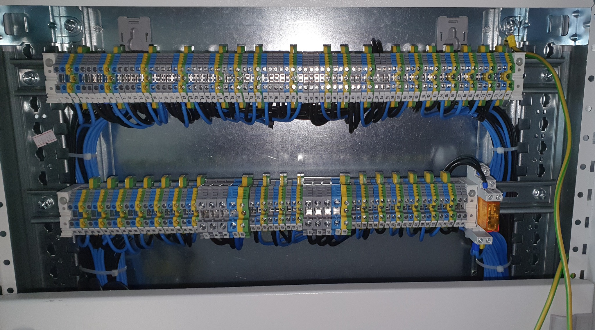 Rozdzielnica elektryczna z dwoma rzędami listew zaciskowych, z podłączonymi przewodami w kolorach niebieskim, czarnym i żółto-zielonym, widoczny przekaźnik i metalowa obudowa z szynami DIN.