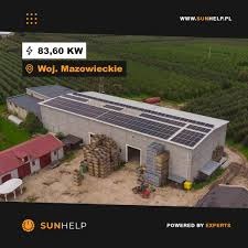 Widok z góry na budynek gospodarczy z zainstalowanymi panelami słonecznymi na dachu, z informacją o mocy 83,60 kW i lokalizacji Woj. Mazowieckie. W tle widoczne drzewa owocowe. Na pierwszym planie...
